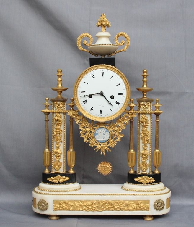 Louis XVI Period Superb and Original Portico Clock with columns and base in white marble, ornated with a Wedgewood Bisquit Plaque and gorgeous Mercury Gilding. Bronze representing grape vines, lyre, quiver with its arrows and the Louis XVI famous