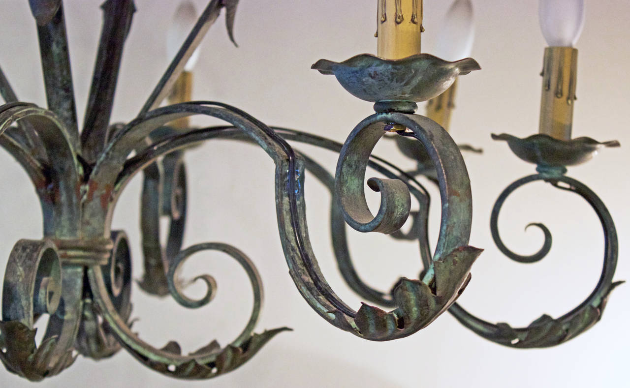 Handsome chandelier with handmade forged iron scrolled arms and top adorned by welded tole acanthus leaves. Painted in a grayish green with a hint of blue. Has been recently rewired for USA std.
Another identical chandelier is available at same