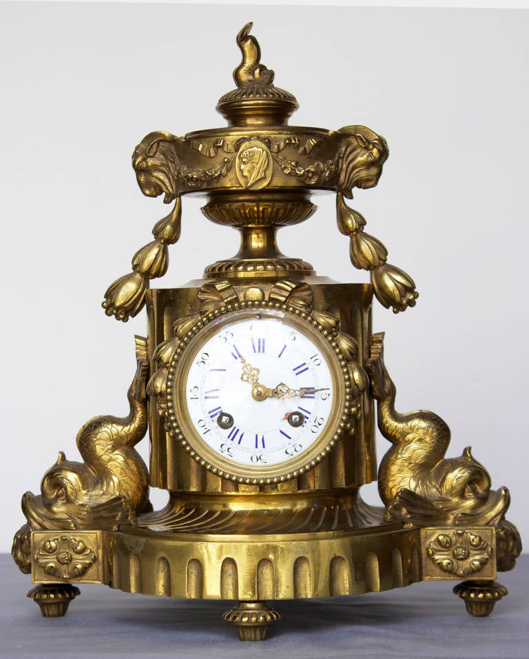 Interesting design with two large stylized dolphins embellished base; a small dolphin is topping the clock and underneath each side shows a Ram's head and a guirland. Also a small medallion of a women's profile in the center top.
Clock has an