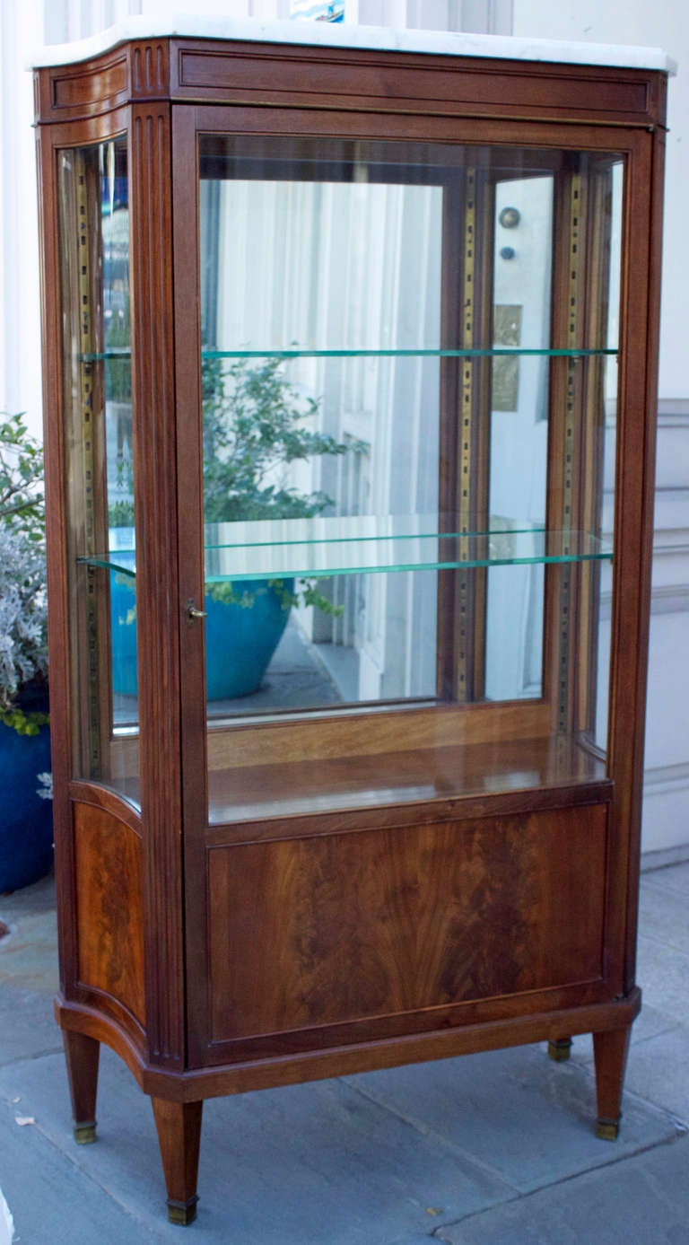 Late 19th century vitrine in solid mahogany with glazed front door and two concave bombe glass sides and nice moldings on top and bottom. The two front and two back pillars are fluted and the cabinet is resting on four pyramidal feet terminated by
