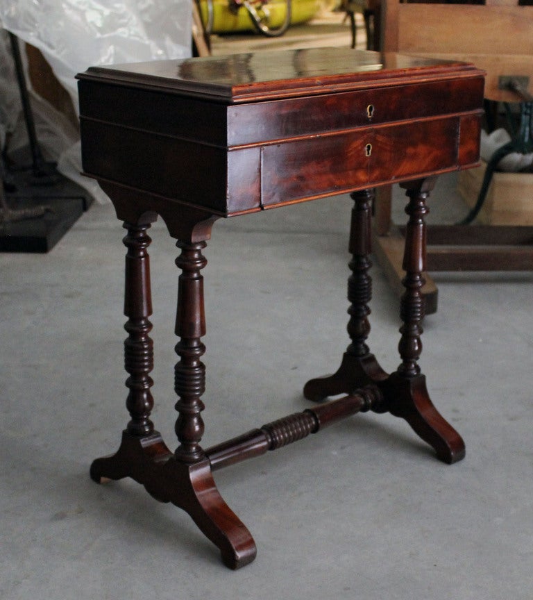Work table in mahogany opening on an interior in clear maple wood revealing a set of five pigeon-holes. A small drawer is situated under. It is supported by two pairs of turned legs resting on 