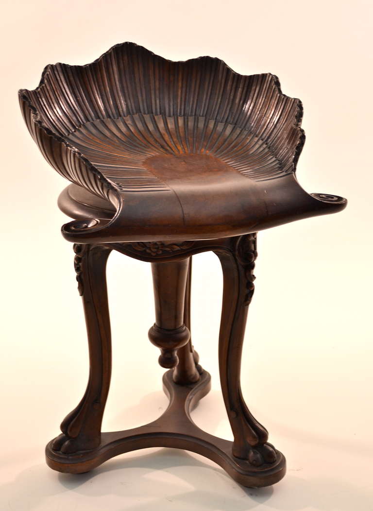 Hand carved with the classic shell motif in fine walnut, a swivel stool with decorated knees and carved paw feet. Beautiful patina.