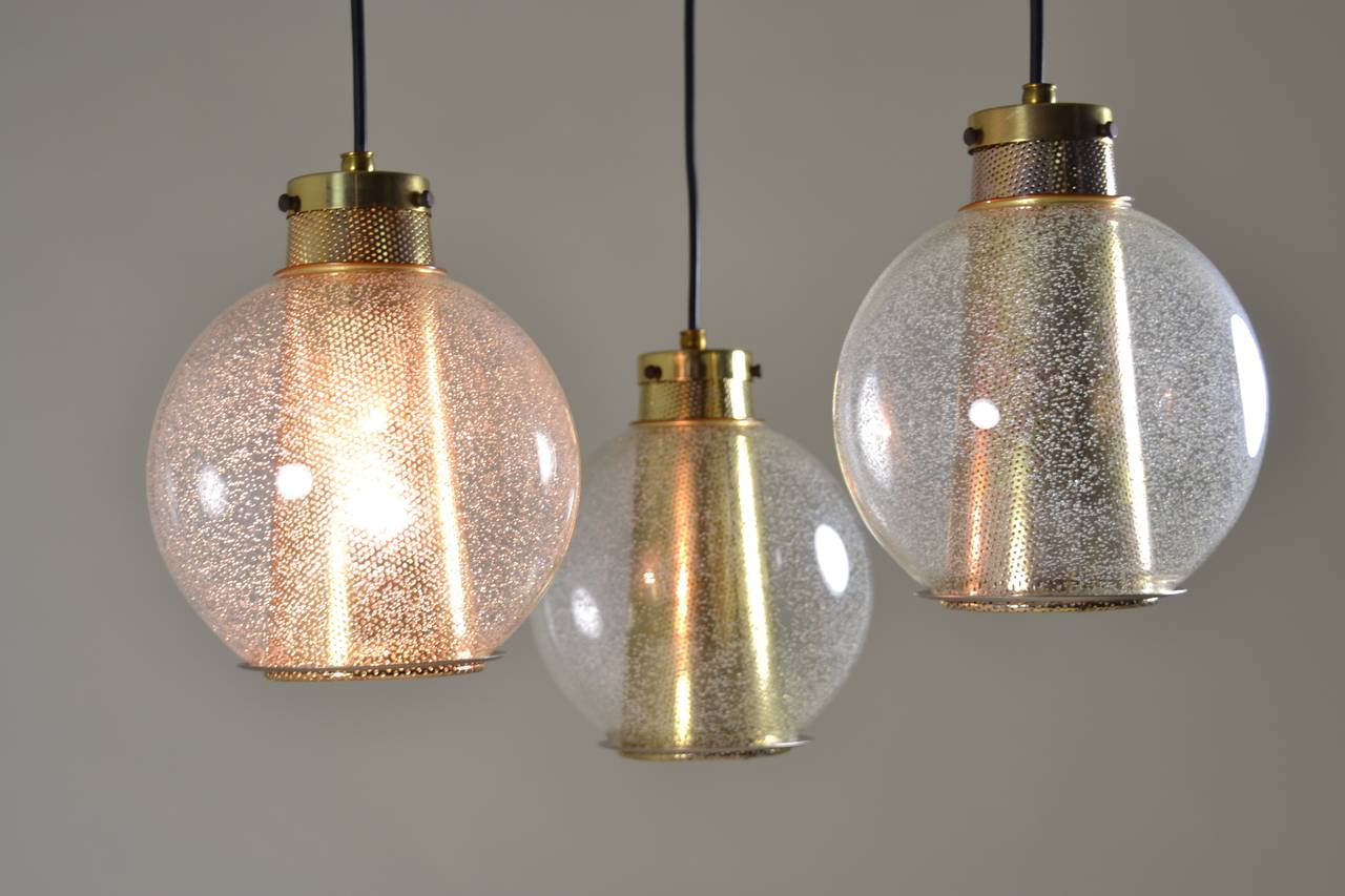 Seeded glass globes over gold metal pierced cones suspended from a Classic modern fixture. Great chandelier, but also would make wonderful individual pendants. All new wiring; length from ceiling and length from fixture to pendants adjustable. Each