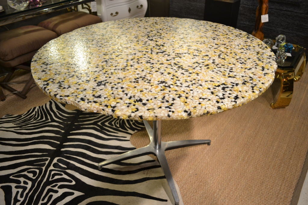Sea shell fragments are suspended in heavy acrylic to form a delightful table top --many shell pieces have a mother-of-pearl sheen. The top is round with four subtle scalloped details evenly spaced around the edge.  It is supported by a simple