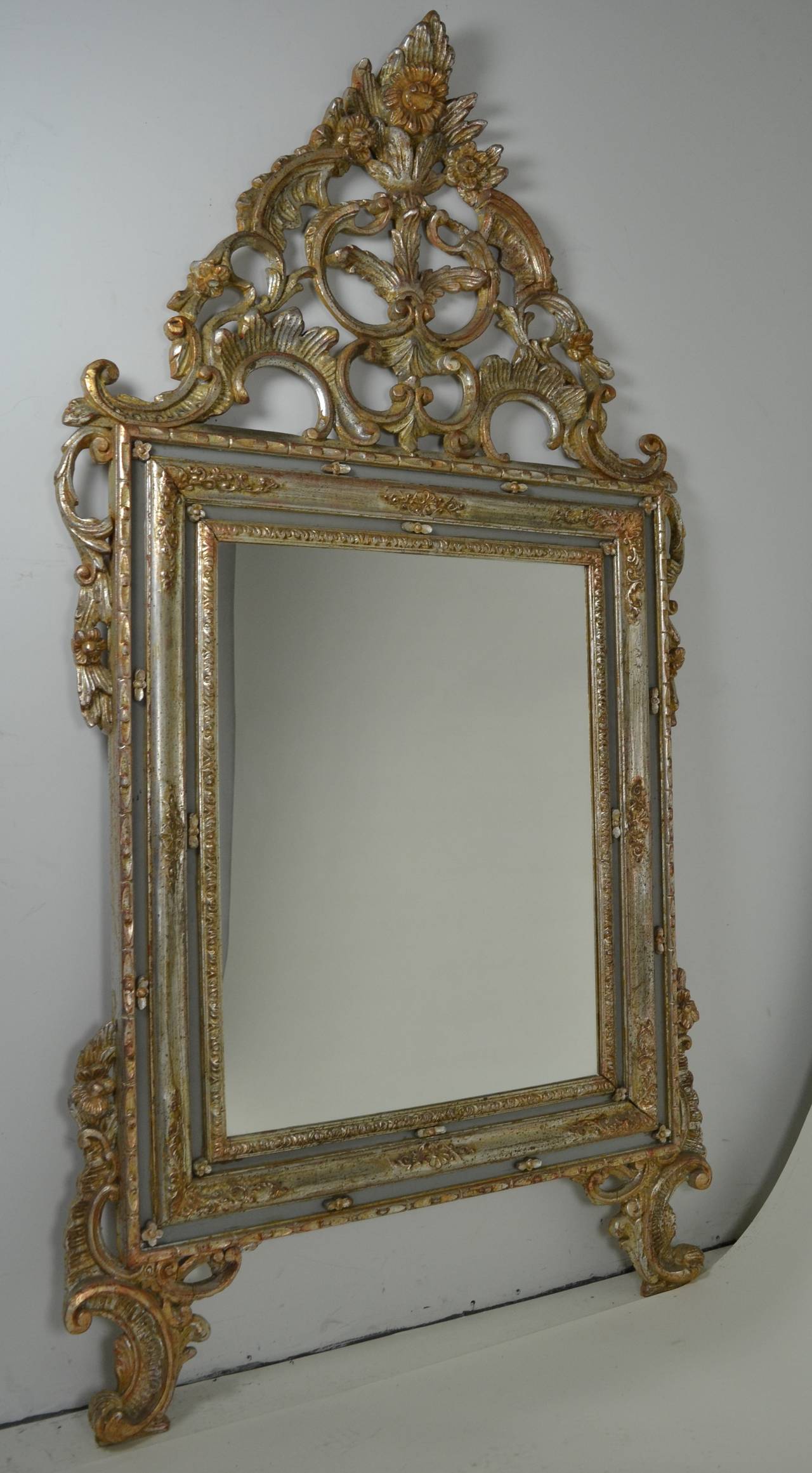 Elaborate carved wood framed mirror in silver and gold gilt. Frosted glass inserts surround the central mirror. Inscribed Made in Italy on verso. Very elaborate crest; almost 6 feet tall.