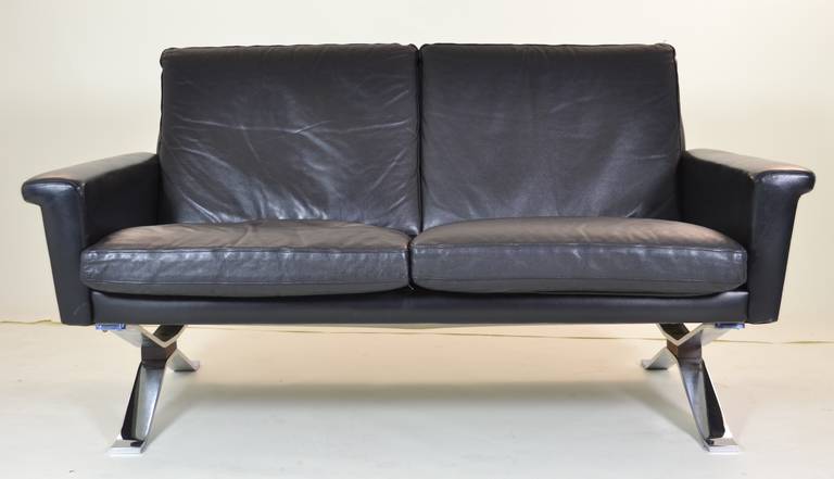 Great form in original black leather cover. Heavy chromed steel legs with teak wood decorative detail. Comfortable and great quality. Generally excellent condition. Note: matching four-seat sofa available in separate listing.