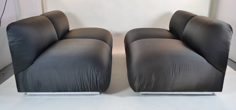 Super sleek and great quality upholstered settees with chrome base detail. Equipped with smooth moving casters. Upholstered in satiny black fabric, in generally excellent condition. Very subtle sun fading on one, circa 1980s.