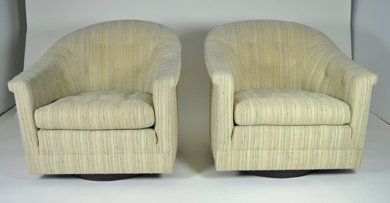 Super quality pair of barrel-back swivel chairs. Circular walnut base houses swivel mechanism. Chairs are heavy and solid. Loose seat cushion. Button tufting detail on back and seat. Vintage cotton fabric is serviceable but worn and should be
