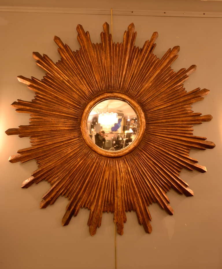 Heavy carved wood sunburst frame in a dark gilt surrounding a convex mirror.