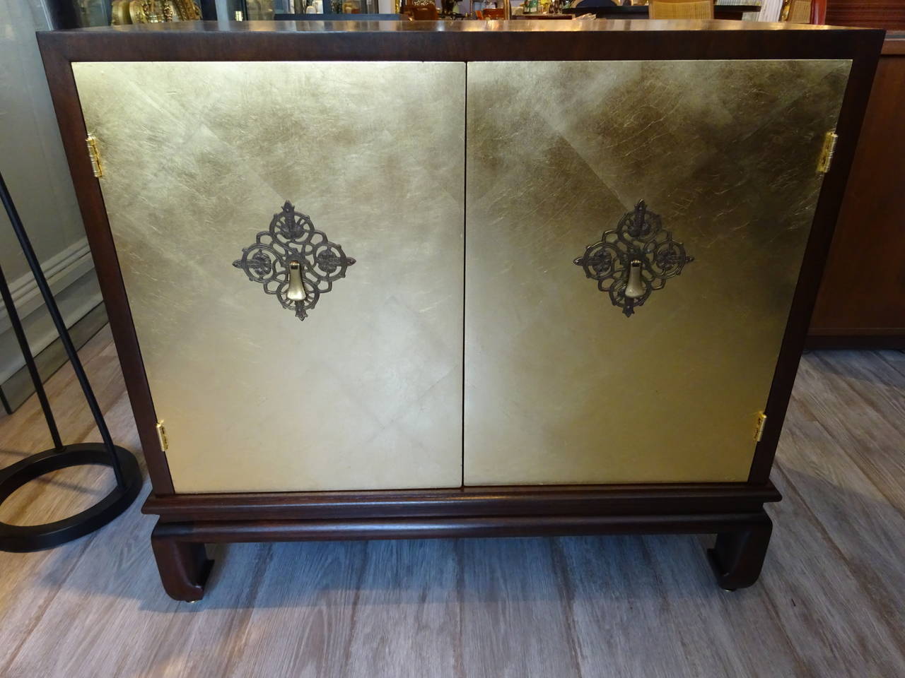 A pair of John Stuart gold leaf cabinets, each one of mahogany with two gold leaf doors, raised on Asian influence bracket base. In two parts. Retains original paper label.