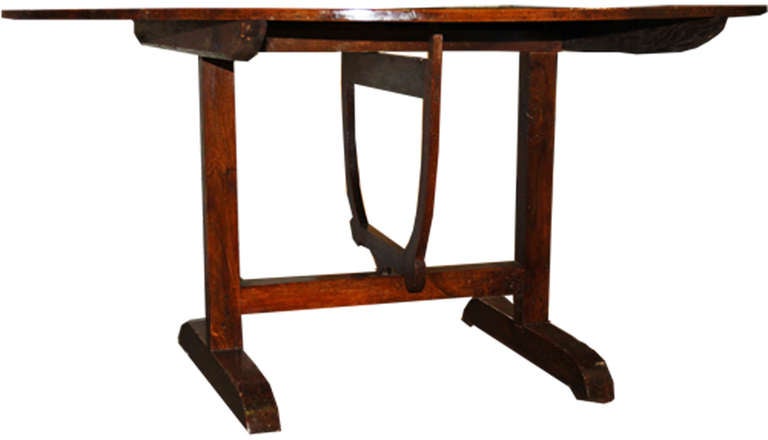 An 18th century French walnut wine tasting table, ovoid in shape and raised on two trestle legs connected by an H-shaped stretcher and a tulip support under the top that serves to tilt the top vertical for ease of storage.