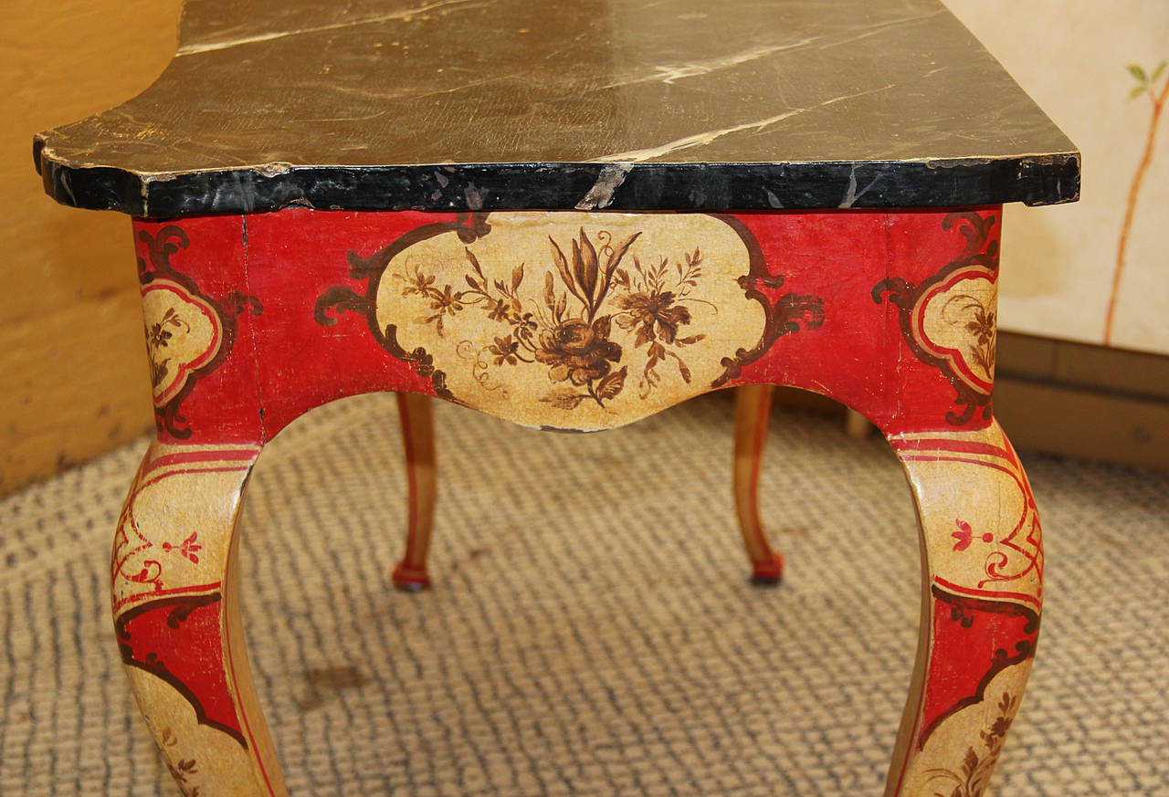 A striking pair of 18th century Venetian polychrome consoles, with faux marble tops, elaborately painted with floral and foliate motifs on a red ground, the whole atop cabriole legs.