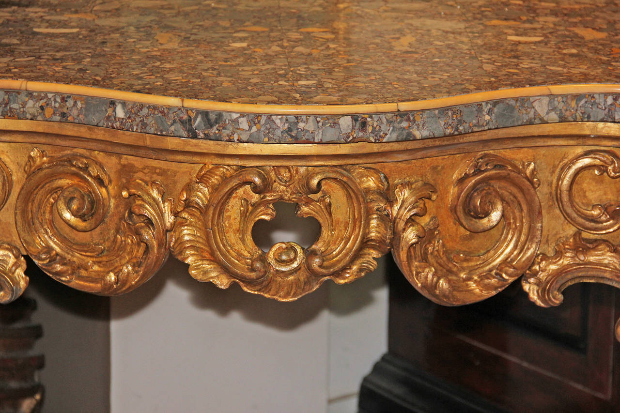 A striking late 18th century Italian Louis XV giltwood console with breccia marble top, accented with siena marble along the edge, the apron carved with rocaille, foliate and shell motifs, the whole resting on four cabriole legs connected by