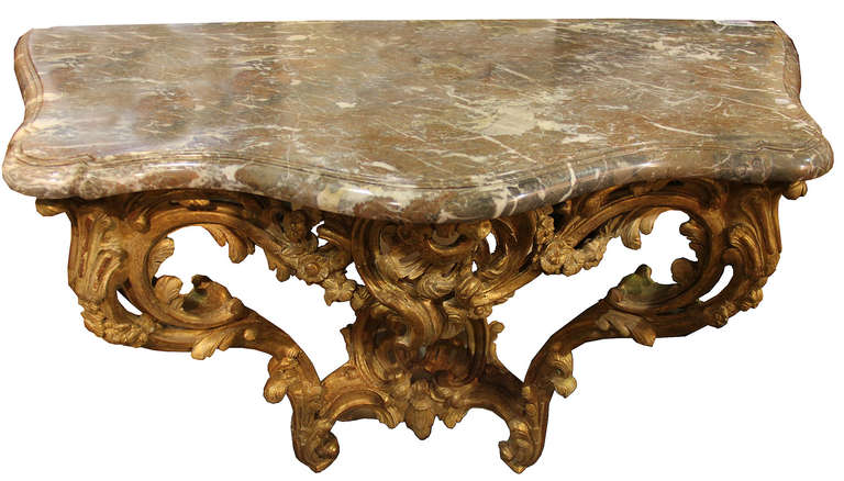 An 18th century French Louis XV giltwood and Brecciam marble console, of serpentine form with a marble top, the frame carved with scrollwork, flowers and foliate motifs.