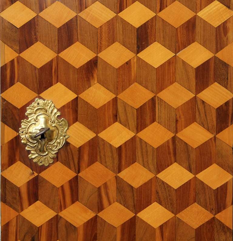 The entire surface dramatically veneered with an intricate pattern of cube marquetry stained to create a trompe l’oeil effect.