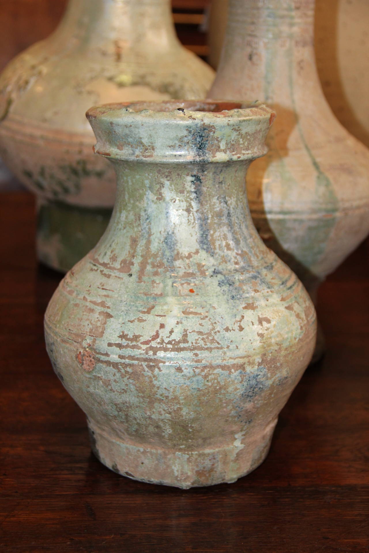 A set of four Han dynasty glazed earthenware jars, of ovoid and waisted form, with shaped mouths, with hints of silvered and glazed in varying green tones of sea foam green, and accented with incised denticulation and geometric forms, used for