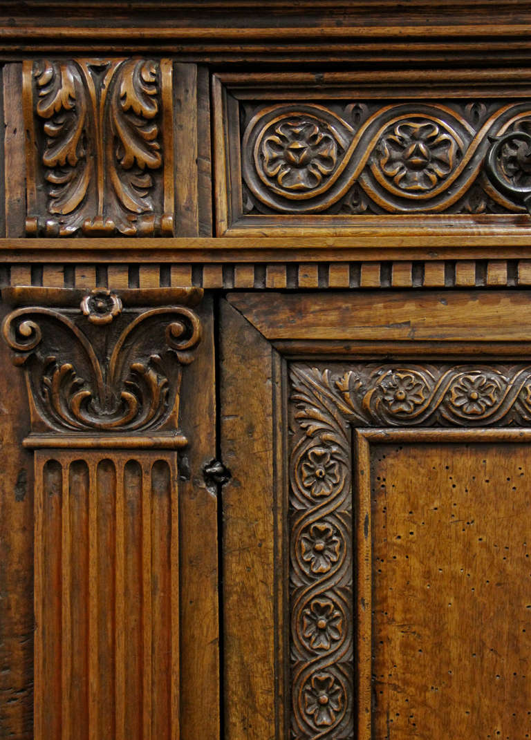 An early 18th century Tuscan walnut credenza, intricately carved with classical architecture elements, the denticulated frieze with two drawers, above two doors highlighted with ornate foliate motifs and flanked by pilasters accented with acanthus