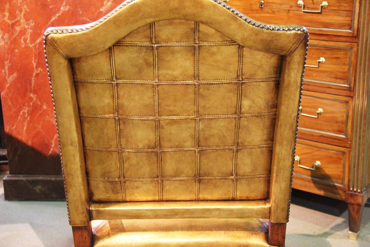 An 18th century Italian walnut fauteuil armchair, now upholstered in 22-karat gilded C. Mariani leather, accented with rosettes and antiqued nailhead trim, with distinctive elongated bec de corbin (bill head)arms raised on turned legs supported by