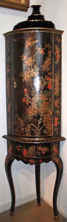 An early 18th century Queen Anne encoignure (corner) cabinet with c-scrolls, floral and foliate decorative motifs japanned in shades of gold, red, and green on a black lacquer field, the whole raised on a conforming stand with cabriole legs