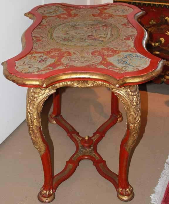 A striking 18th century Italian Rococo vermillion polychrome and parcel-gilt Venetian petit point-topped side table, the serpentine frame inset with the intricate hand needlework depicting floral and foliate motifs centered with an aristocratic fête