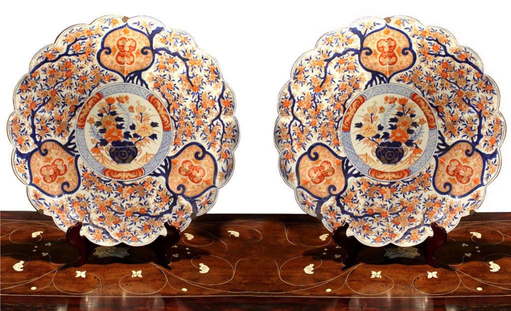 A monumental pair of late 19th century Japanese porcelain Imari chargers, Meiji Period (1868-1912), of shallow scalloped form, each decorated with a profusion of branches full of cherry blossoms encircling a vase containing chrysanthemums, lotus and