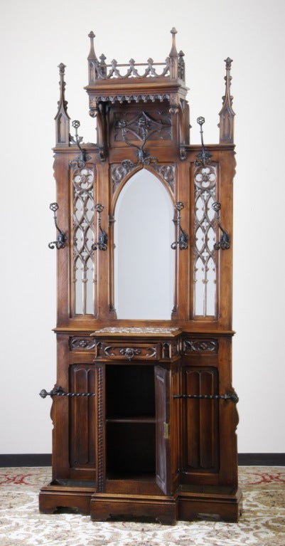 19th century French Gothic Revival carved walnut hall tree relief carved with quatrefoil designs and linen fold panels, the central beveled mirror flanked by original wrought iron coat and hat hooks and wrought iron umbrella holders.