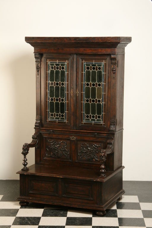 Unique 19th century 2-part English quarter sawn oak Jacobean-style hall bench bookcase with leaded glass doors, lift top seat, and hidden storage compartment behind a drop front carved panel.