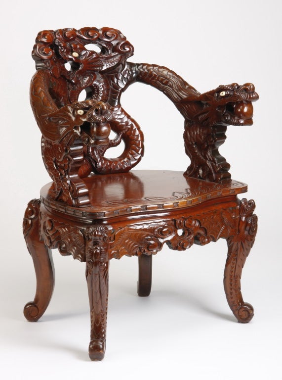 20th century Chinese carved arm chair, the back depicting a dragon in profile chasing the illusive pearl of wisdom, with dragon form arms decorated with ivory eyes, the solid seat over an apron with stylized clouds, 34