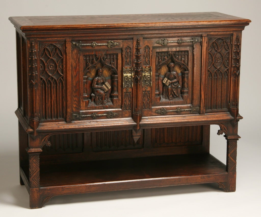 19th century English pollard oak Gothic Revival double door server with relief carved doors depicting the lord and lady of the manor, flanked by carved linen fold panels, all surmounted by an lower open display shelf.