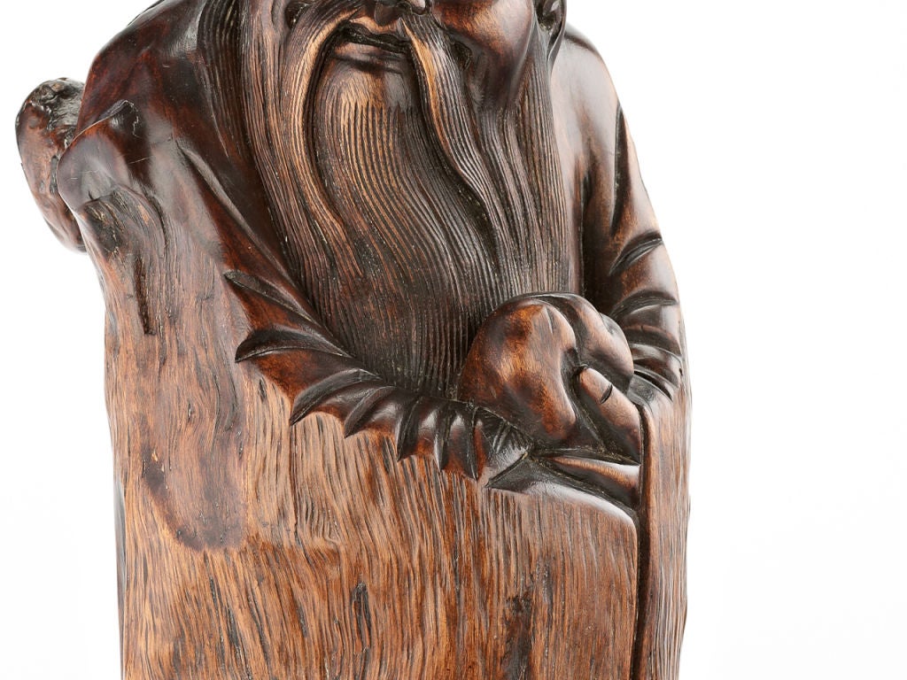 A cylindrical section of root-wood carved in the form of Shoulao wrapped in a coat formed by the gnarled skin of the wood, the wise man recognizable by his protruding forehead and long beard, holding a peach in his hand. 

Shou Lao is the God of