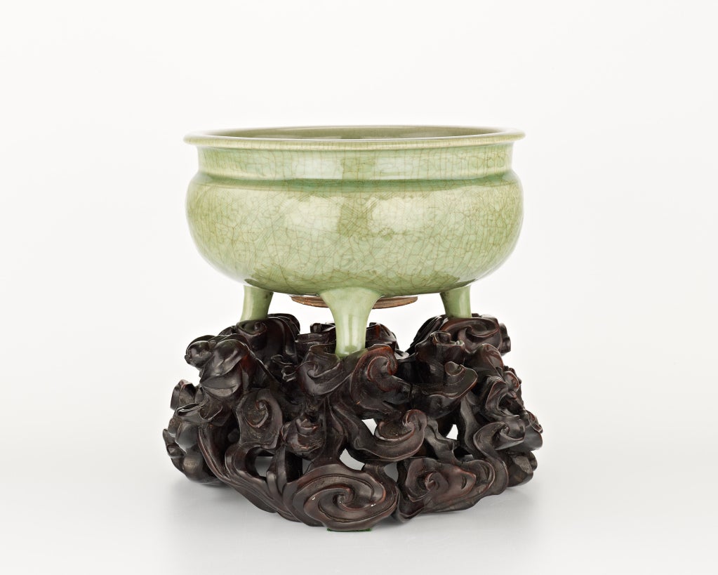 A large longquan-ware celadon censer raised on three feet, the outside decorated with an incised geometrical design beneath a crackle-glaze, together on a later wood stand elaborately carved with bats and scrolling clouds.