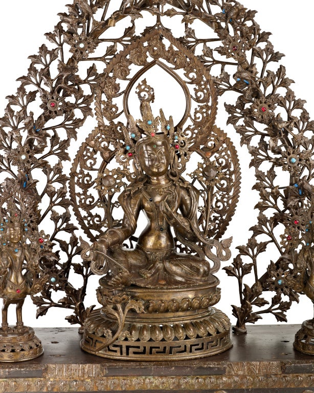 The Goddess Tara in the center seated in lalitasana pose on a lotus throne, two Kinnara censers on either side performing the vitarka mudra, wood stand with a large multi-part floral mandala crowned by ribboned canopy.

Tara is a female