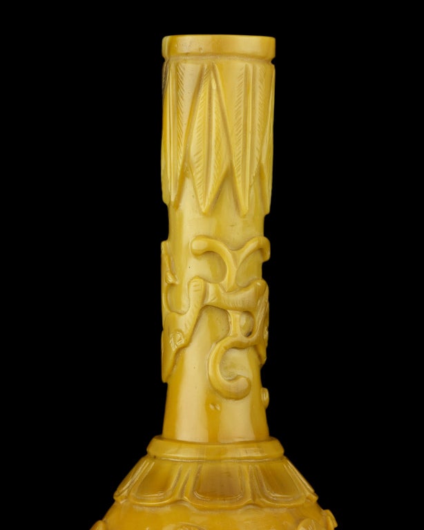 A small bottle vase of pear-form with a tall, narrow cylindrical neck, possibly a water dropper, the glass of opaque brownish-yellow sandwiched glass carved with a peacock beside a peony and another peacock beside a pine tree, the base with a