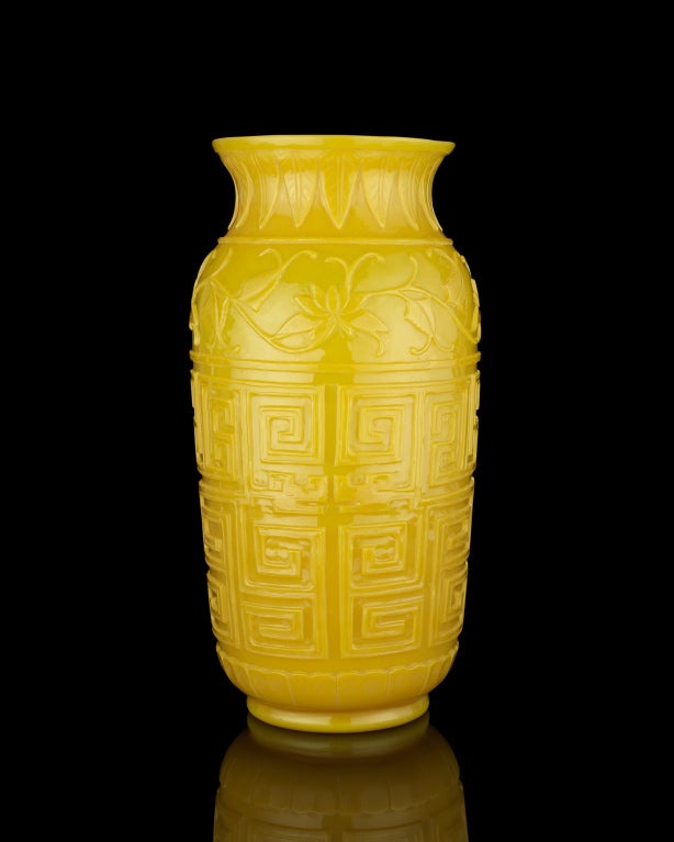 A large opaque yellow glass vase of mallet form with a slightly recessed foot, the body carved with a geometric design of archaistic qilong beneath a garland of lilies and leaves, the wide flaring mouth carved with a band of banana-leaf