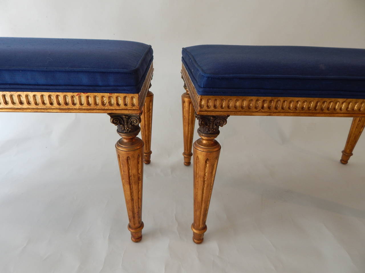 Mid-Century 1950s /1960s gorgeous pair of gilded wooden decorative benches with carved detail. Acquired from a well-cared for estate. Both are in excellent original condition. Original blue upholstery is in excellent condition.