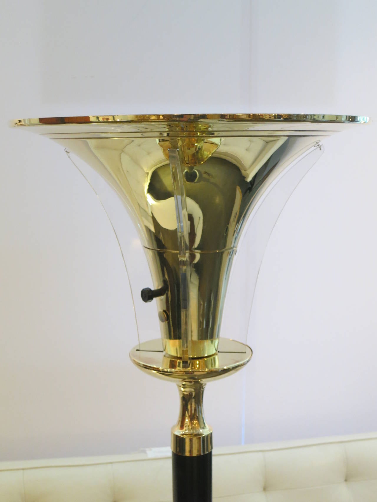 A classic pair of uplights with  brass, trumpet shaped shades and brass accents. The upright column and disc base are an ebonized metal. Four lucite leaves surround each brass shade and heighten the glamour of the lamp. Each torchiere has a single