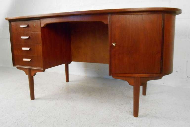 Stylish Scandinavian modern design of this kidney shaped teak desk with shelf/pass through storage compartment on back side makes a striking piece in home or business office. Mid-Century teak finish adds to the vintage appeal of this Danish modern