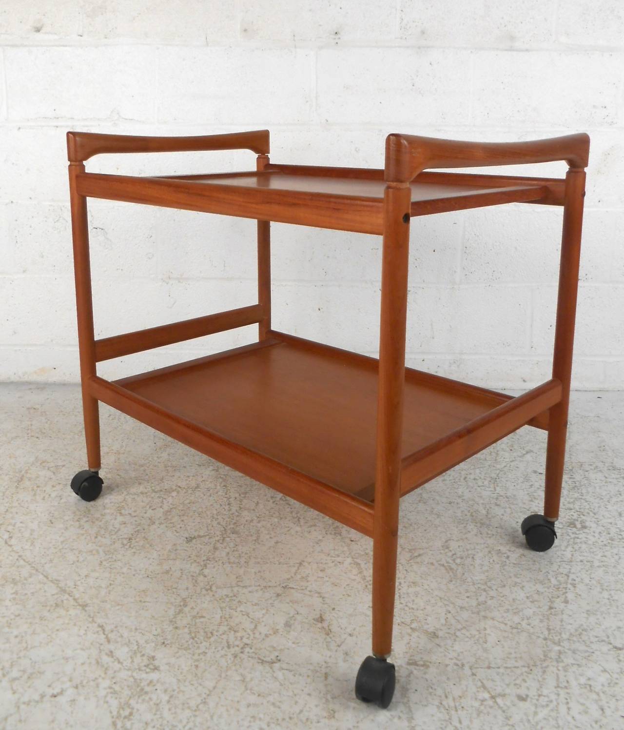 Vintage rolling tea/bar cart, made of sculpted teak wood with two levels, set on 360 degree wheels. Smooth formed handles, great Danish style. Makes for a great movable console or side table.

(Please confirm item location - NY or NJ - with
