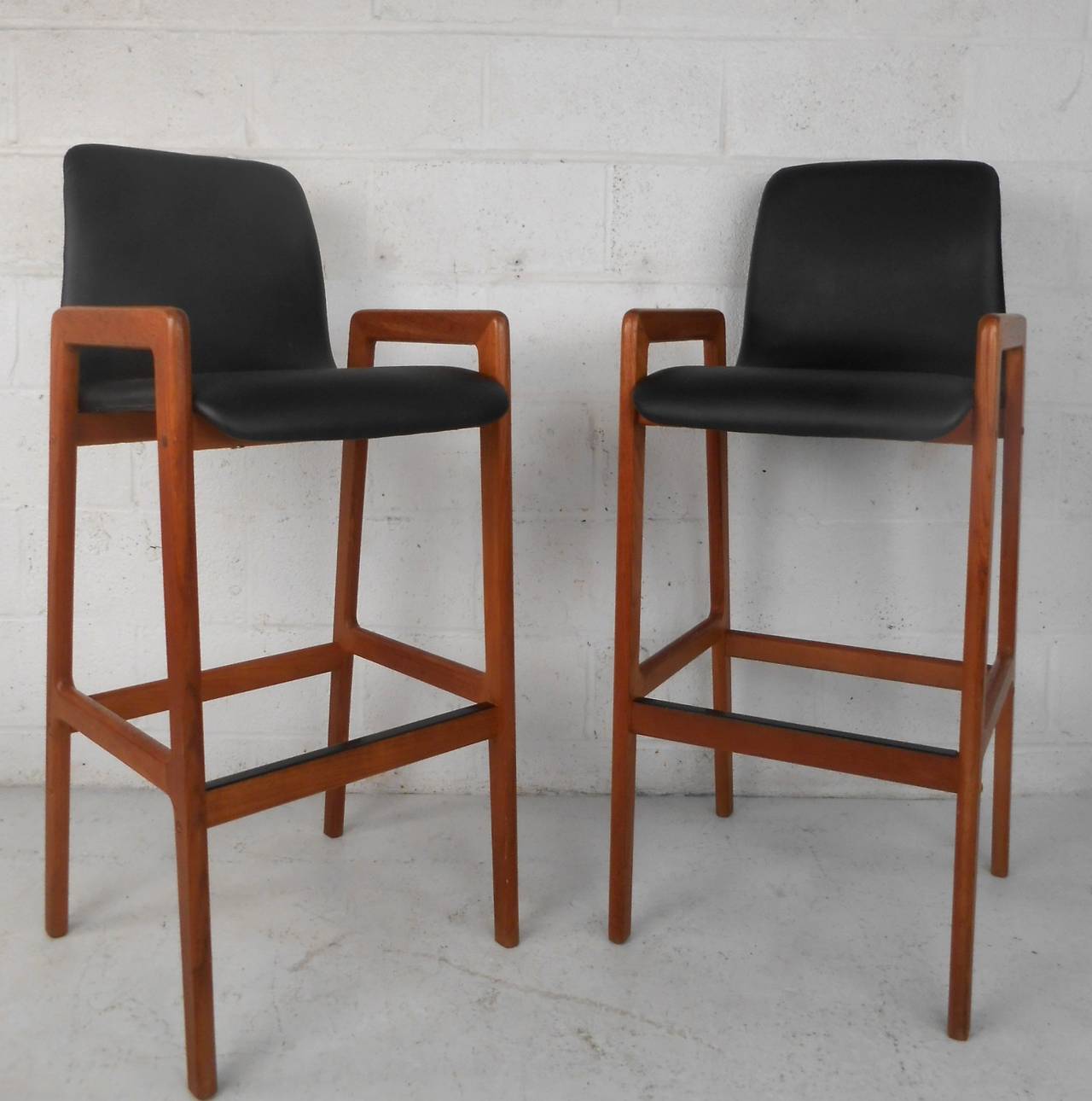 This pair of mid-century teak stools feature comfortable full size seat backs paired with complementary arm and foot rests. Quality vinyl covering and classic  Danish teak construction make these a great fit for any  home or business. Please confirm