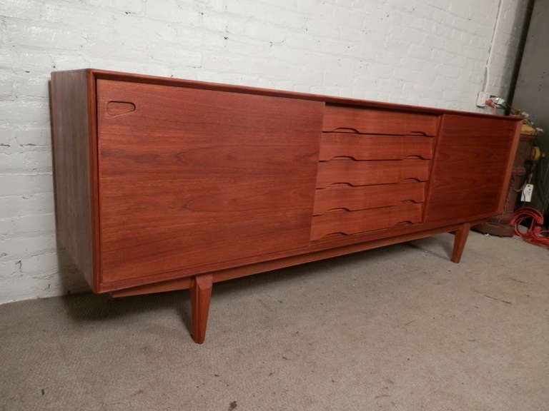 Beautiful Danish server with long clean lines, angular sculpted legs, streamlined handles on the drawers and the inset door handles. Tons of storage space inside and all of the shelves are adjustable. The backside is finished making this piece