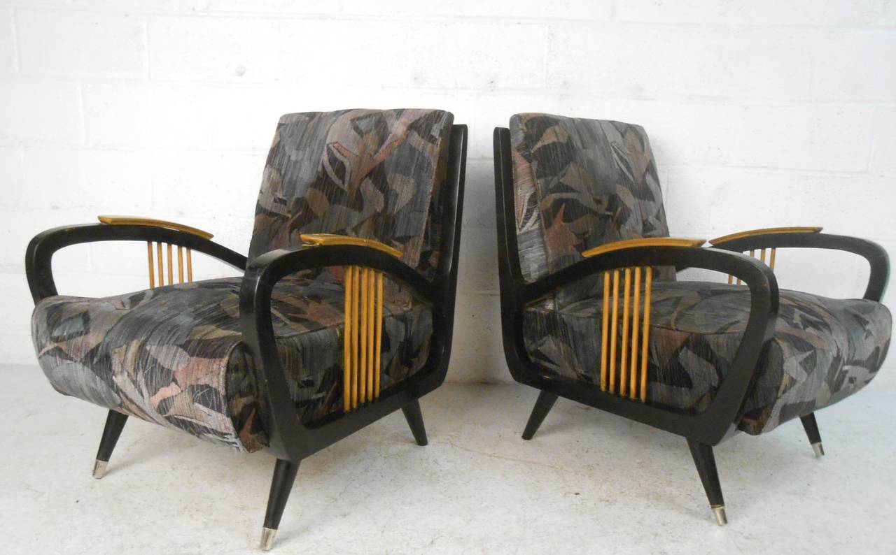This pair of mid-century armchairs feature striking ebonized frames with unique blonde spokes, tapered legs, and vintage covering. In need of some restoration, this pair adds a visually striking seating option to any interior. Please confirm item