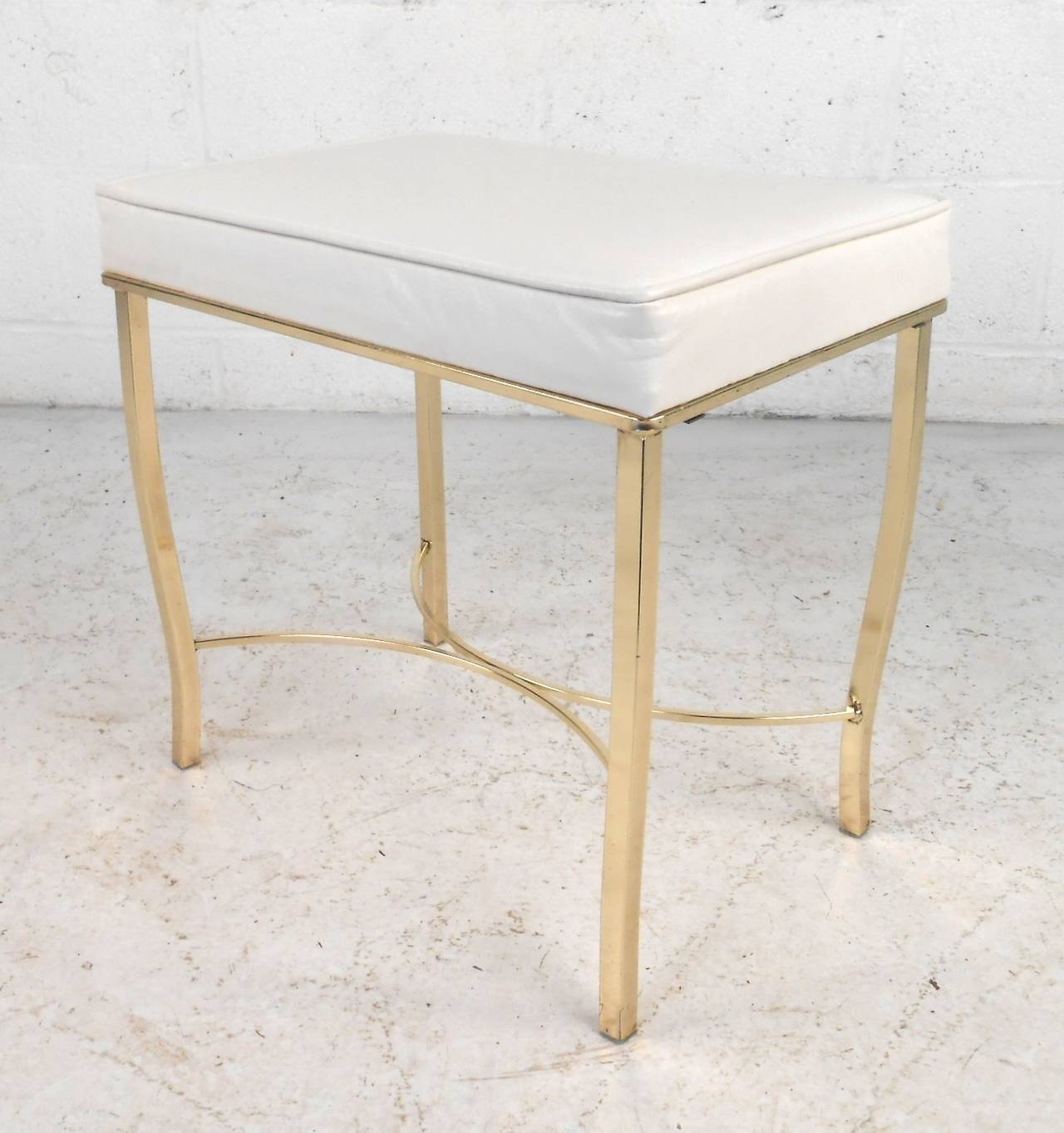 Mid-century modern ottoman/stool with white vinyl and metal frame. Attractive polished brass curved legs and stretcher accent the white fabric seat.

(Please confirm item location - NY or NJ - with dealer)