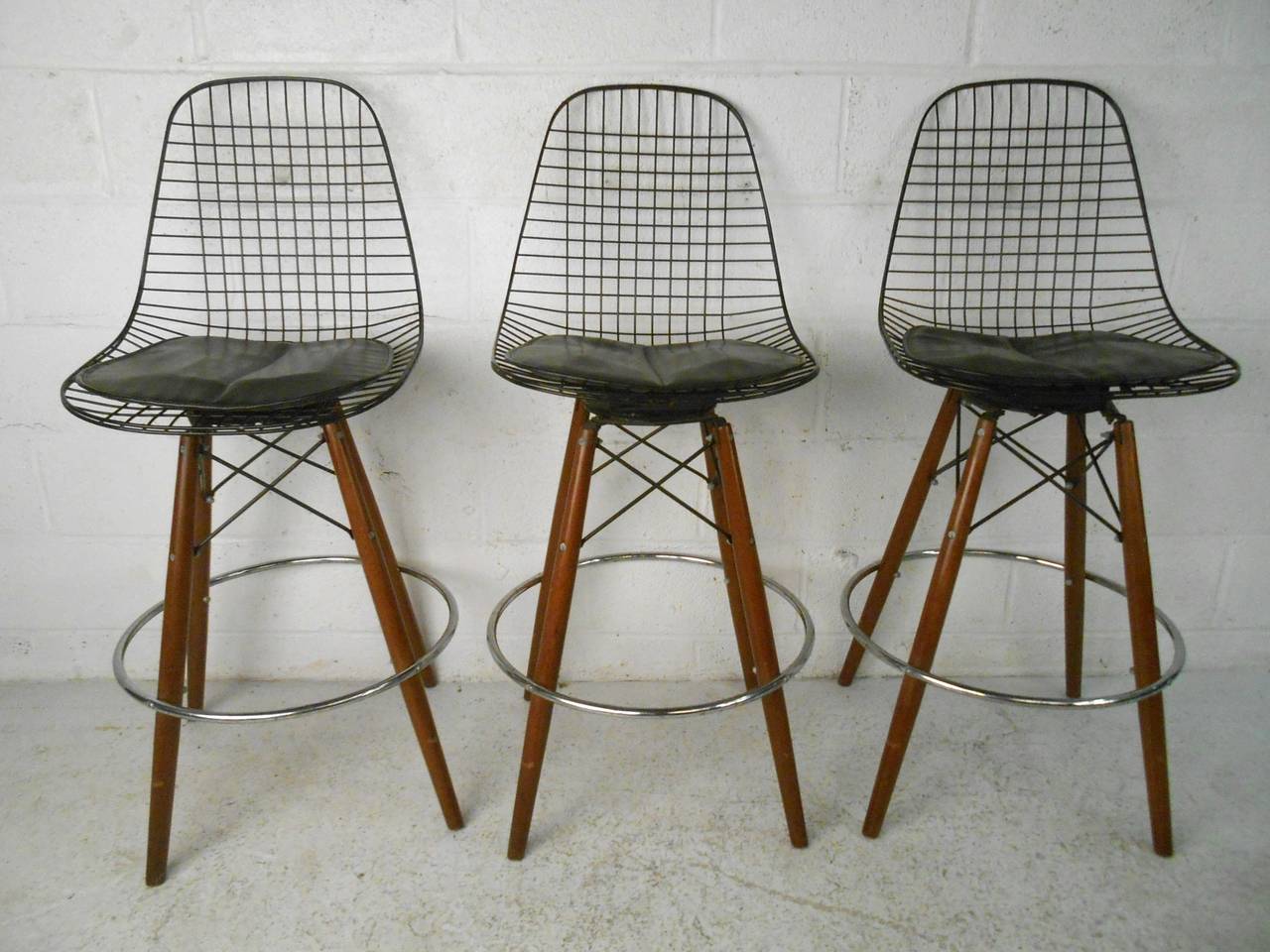 This set of vintage barstools meshes swiveling metal seat frames with tapered wooden legs to create a striking addition to any bar setting. Stretchers and chrome footrest offer added stability to the seats, while leather padding provides added
