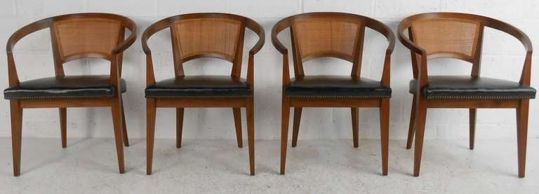 Set of four Baker Furniture chairs with cane backs, black vinyl seats with decorative nail heads, and walnut frames. Very elegant statement.Please confirm item location (NY or NJ) with dealer.