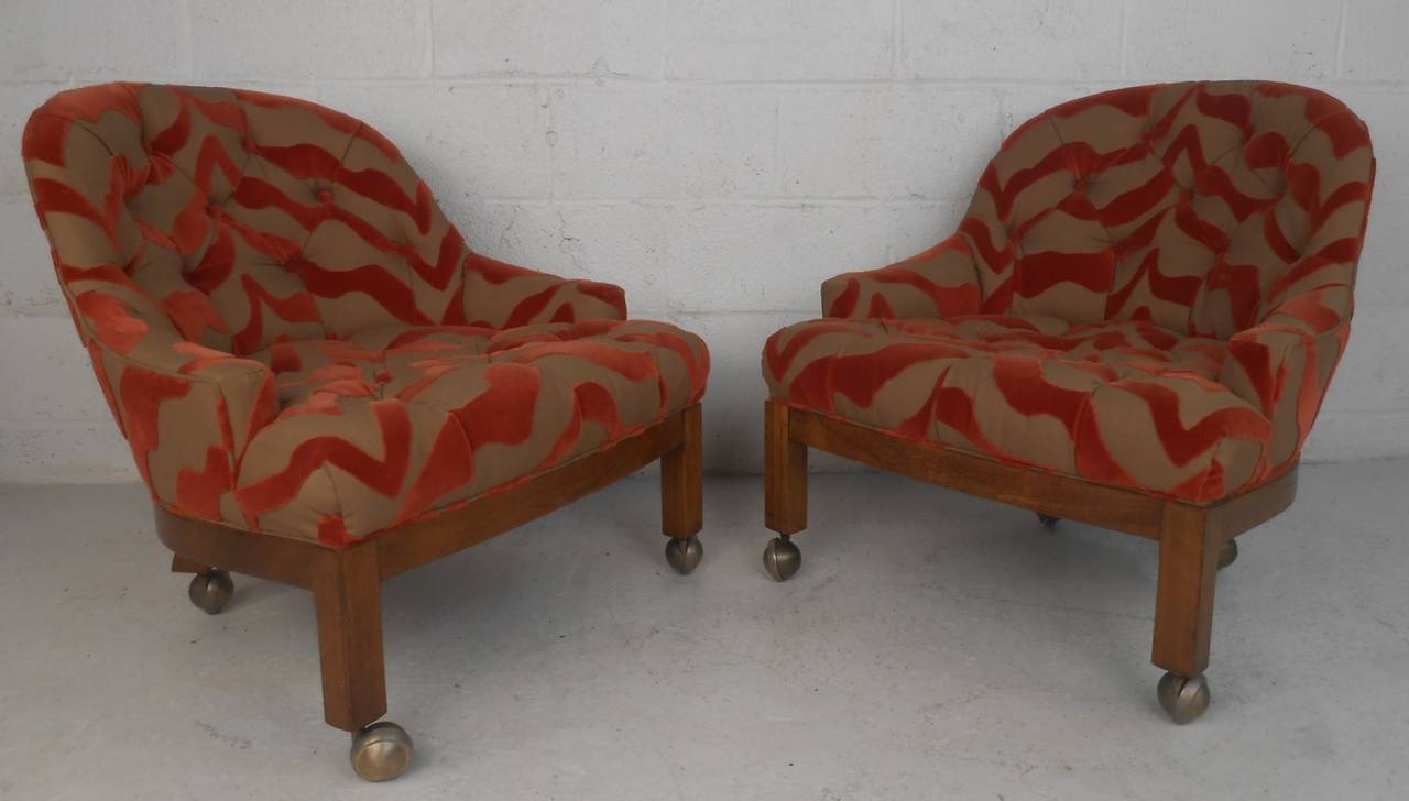Pair of matching midcentury lounge chairs with walnut frames, brass-plated casters, and unique patterned tufted upholstery. Comfortable vintage chairs perfect for home or business seating. Please confirm item location (NY or NJ) with dealer.