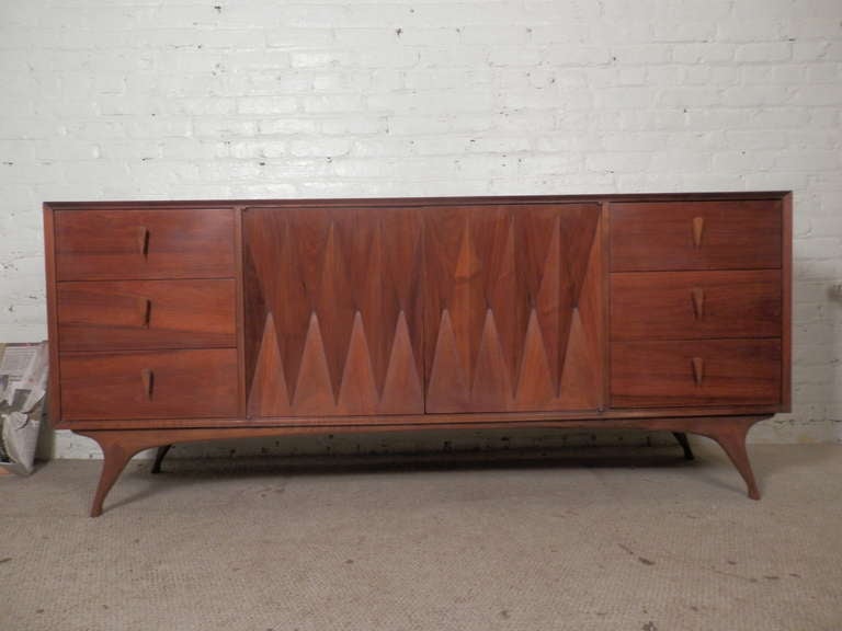 Wild mid-century design with sculpted front and tear drop wood pulls, beautifully angled legs and nine drawers. The shaped cabinet doors open easily with push catch latches as well as the drawers which run on metal slide tracks.
All of this adds up