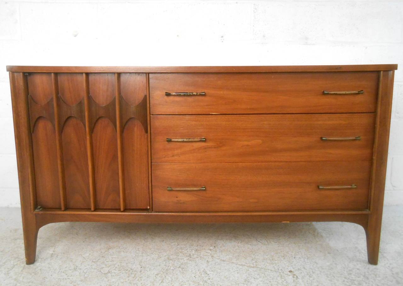 Unique sculpted cabinet door with Kent Coffey style design make this short credenza an attractive midcentury addition to any interior space. Mixture of cabinet and drawer storage make this perfect for stylish organization. Please confirm item
