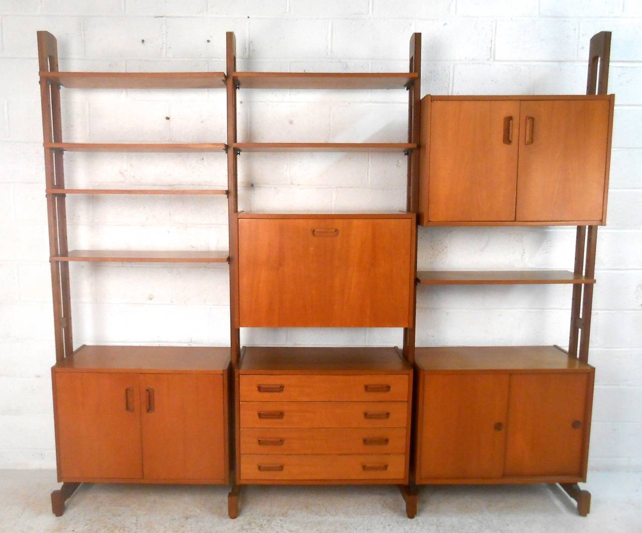 This beautiful Mid-Century teak unit features unique sculpted pulls, feet and frames. Freestanding design and finished back make this suitable for use against a wall or as room divider. Drop-leaf center cabinet compliments traditional drawers and