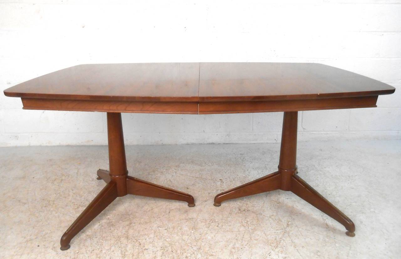 This unique midcentury walnut dining table is set on two sturdy industrial style metal pedestal legs. Additional leaf extends width from 63.5