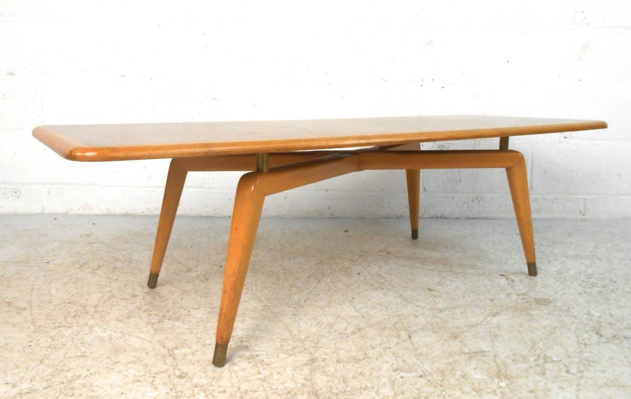 This vintage coffee table features stylish mid-century design, complete with two-tone construction and wonderful brass trim. From metal capped feet to the spacers that elevate the top from the x-style legs, this piece adds character and style to any